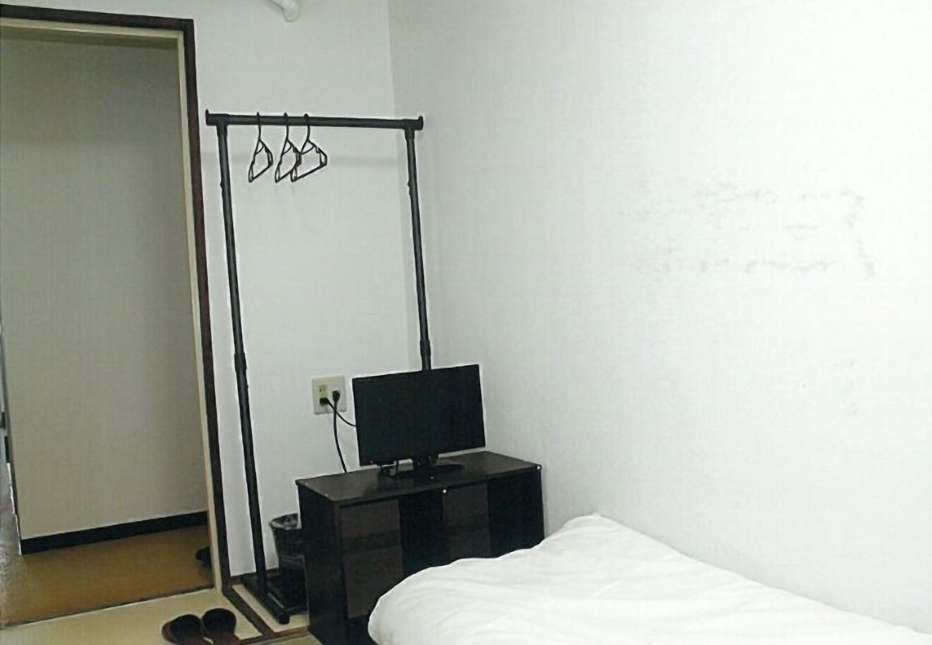 A bedroom with a bed, a TV on a stand, a clothes rack, and a door.