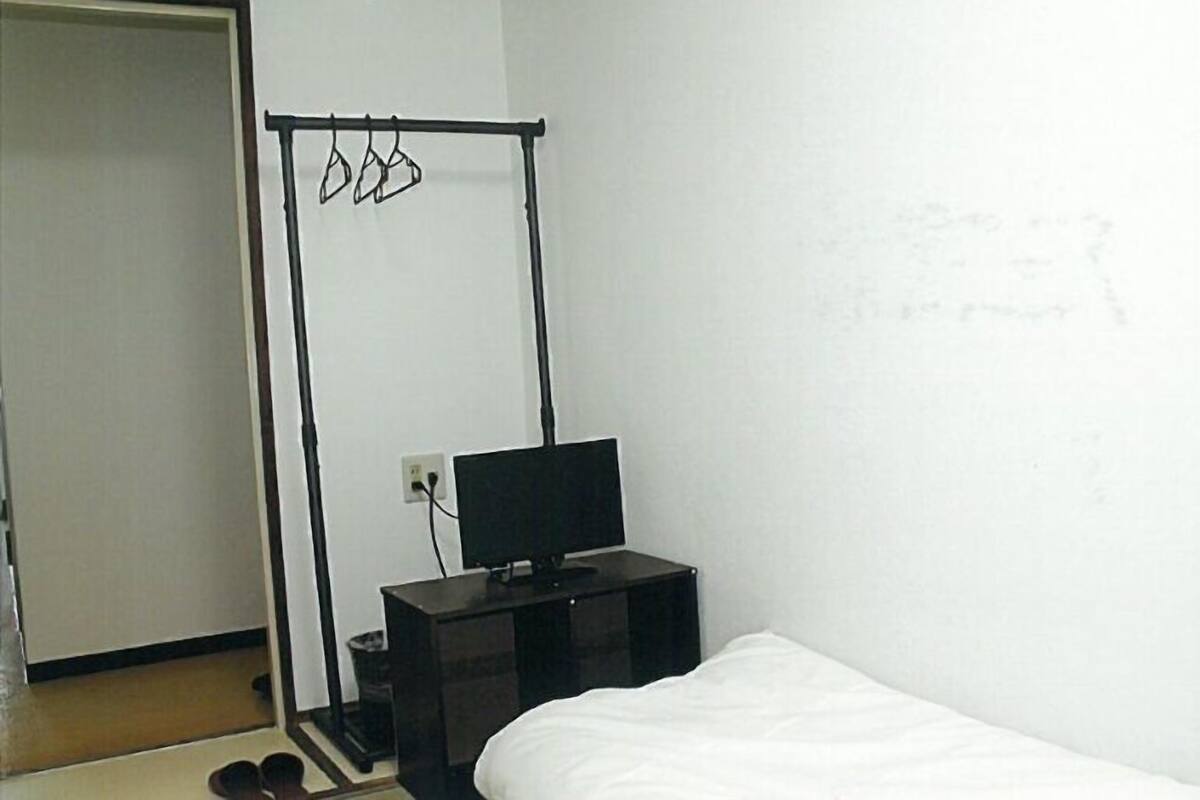 A bedroom with a bed, a TV on a stand, a clothes rack, and a door.