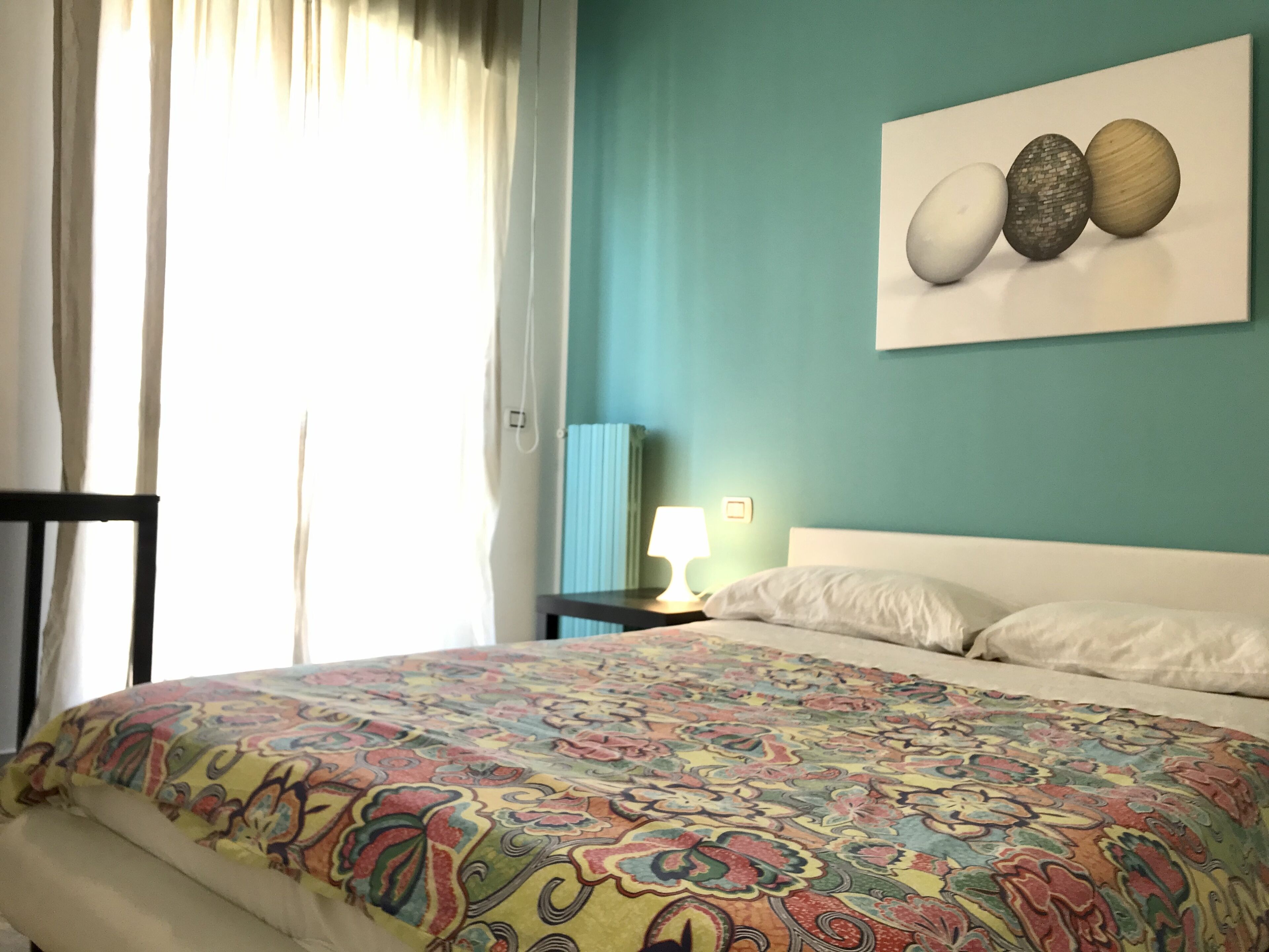 A bedroom with a bed, a nightstand, a lamp, and a wall-mounted artwork.
