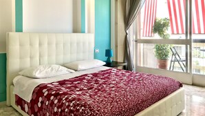 Quarto com uma cama grande, mesa de cabeceira, abajur e janela com cortinas.