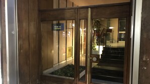 Uma entrada de madeira com uma placa indicando SALA 110, um 6º andar, e uma escada que leva para dentro.