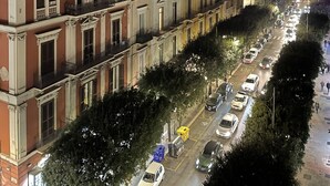 Vista noturna de uma rua urbana com edifícios históricos, apresentando uma variedade de estilos arquitetônicos e uma via aberta com carros estacionados.