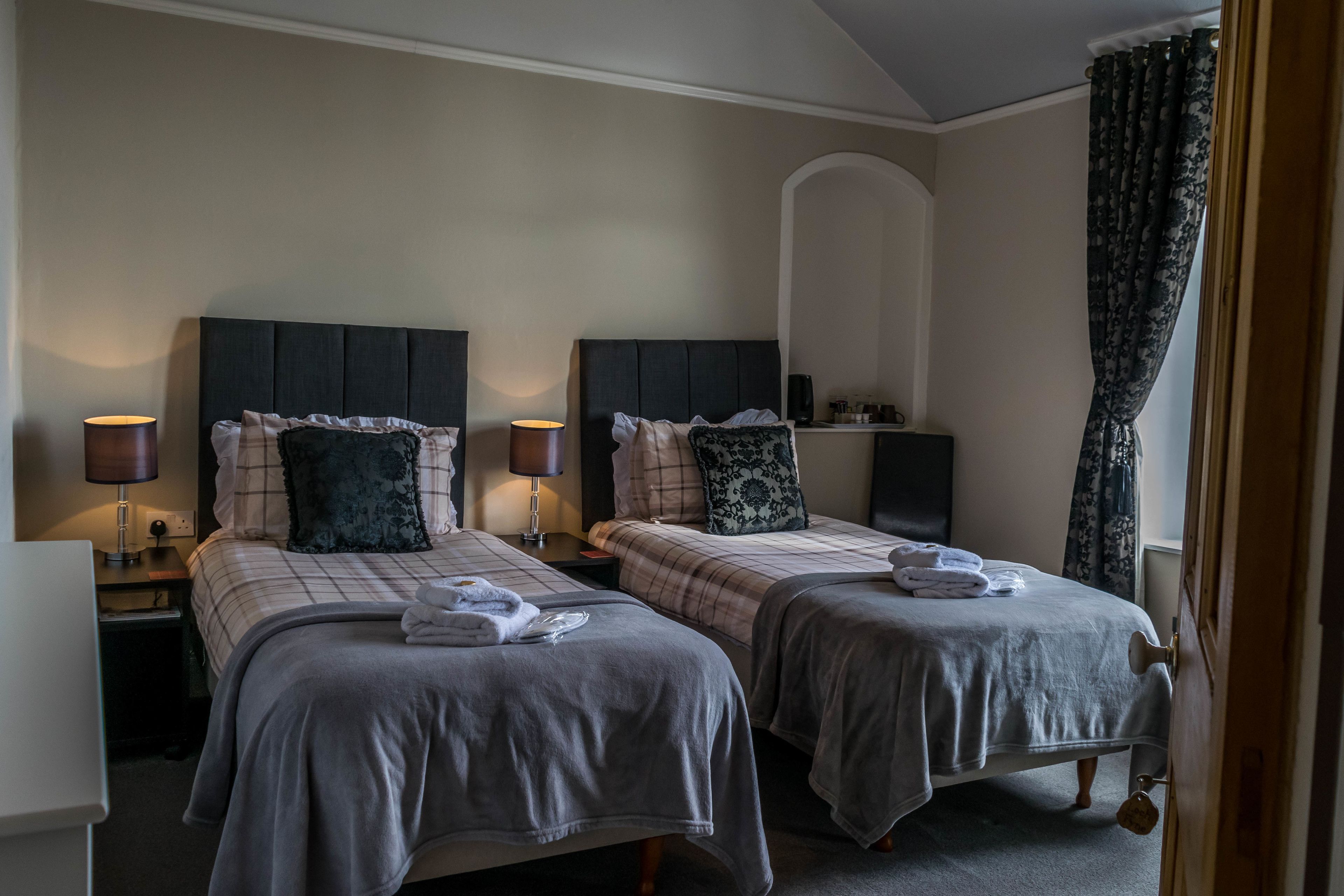 Ett hotellrum med två sängar, var och en med en sänggavel, sängbord, lampor och prydligt hopvikta handdukar.