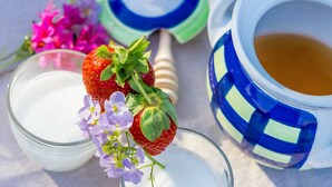 A glass jar with a strawberry and flowers, a honey dipper, and a blue and white ceramic pot with a liquid. - Tregortha (Tighnabruaich)