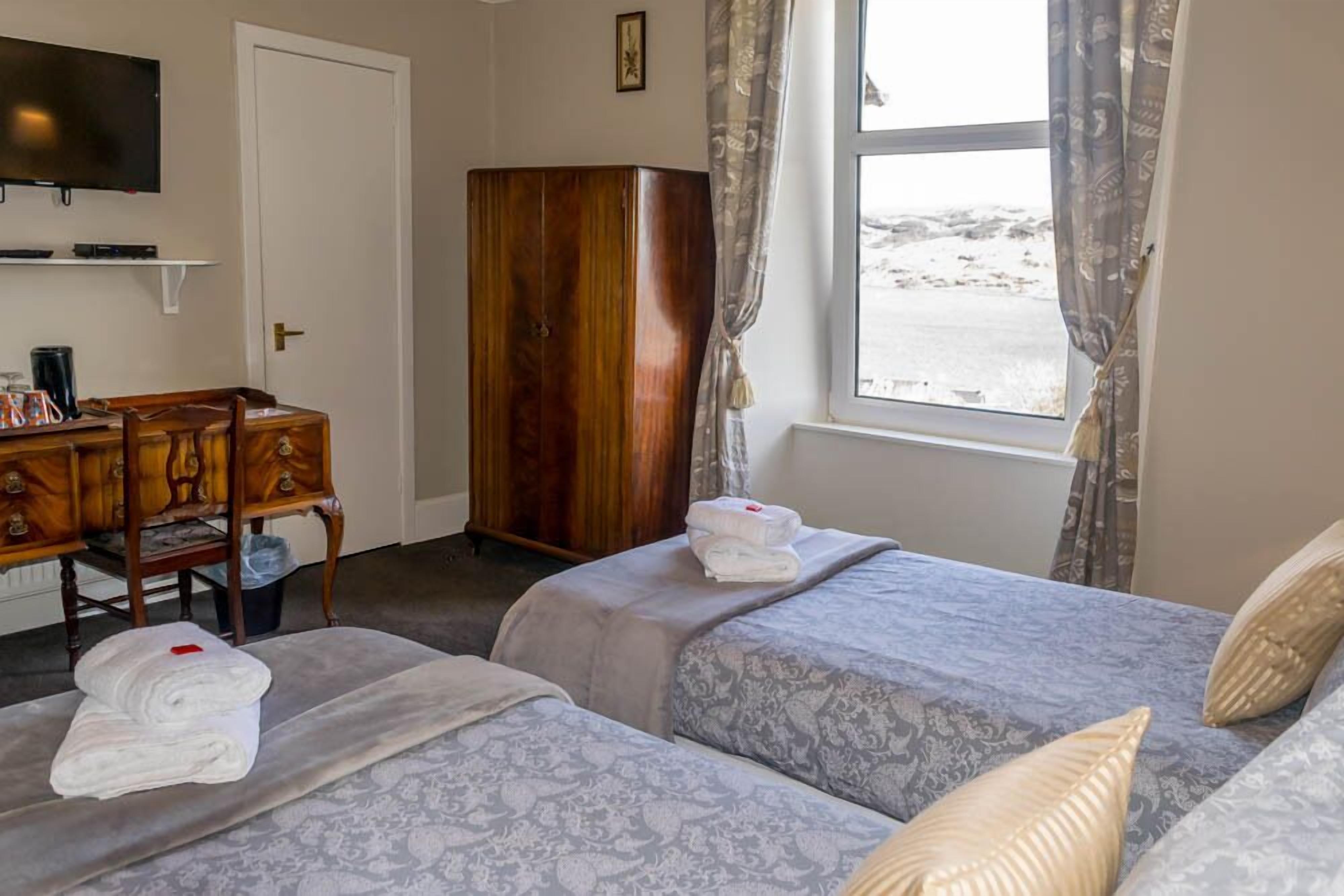 Een hotelkamer met twee bedden, een houten garderobe, een bureau met stoel, een televisie en een raam met gordijnen.