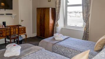 Een hotelkamer met twee bedden, een houten garderobe, een bureau met stoel, een televisie en een raam met gordijnen.