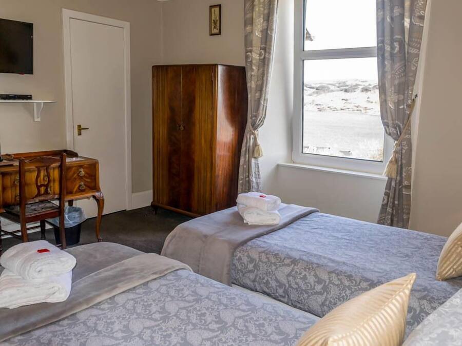 Een hotelkamer met twee bedden, een houten garderobe, een bureau met stoel, een televisie en een raam met gordijnen.