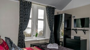 A hotel room with a bed, a TV, a dresser, and a window with curtains. - Tregortha (Tighnabruaich)