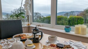 A breakfast table with plates of food, a coffee pot, and a view of the outdoors. - Tregortha (Tighnabruaich)