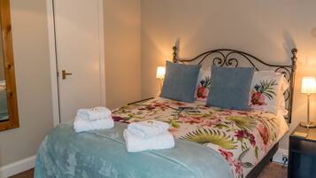 Una cama bien hecha con ropa de cama floral, dos almohadas y toallas dobladas sobre un cabecero.