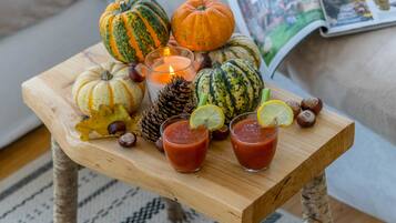 Una mesa de madera con varias calabazas, una vela, piñas y dos vasos de un brebaje rojo adornado con lima.