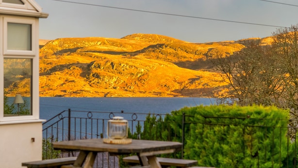 A wooden picnic table with a lantern, a view of a lake, and a mountainous landscape. - Tregortha (Tighnabruaich)