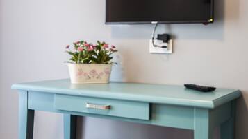 Un escritorio azul verdoso con una planta en maceta, un control remoto y un televisor fijado a la pared.