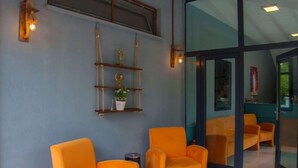A room with orange chairs, a wall-mounted shelf with decorative items, and a glass partition.