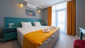 A hotel room with a large bed, a teal headboard, a yellow blanket, a red chair, and a painting on the wall.