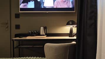 Una habitació d'hotel amb llit, escriptori amb làmpada, cafetera i televisió penjada a la paret.