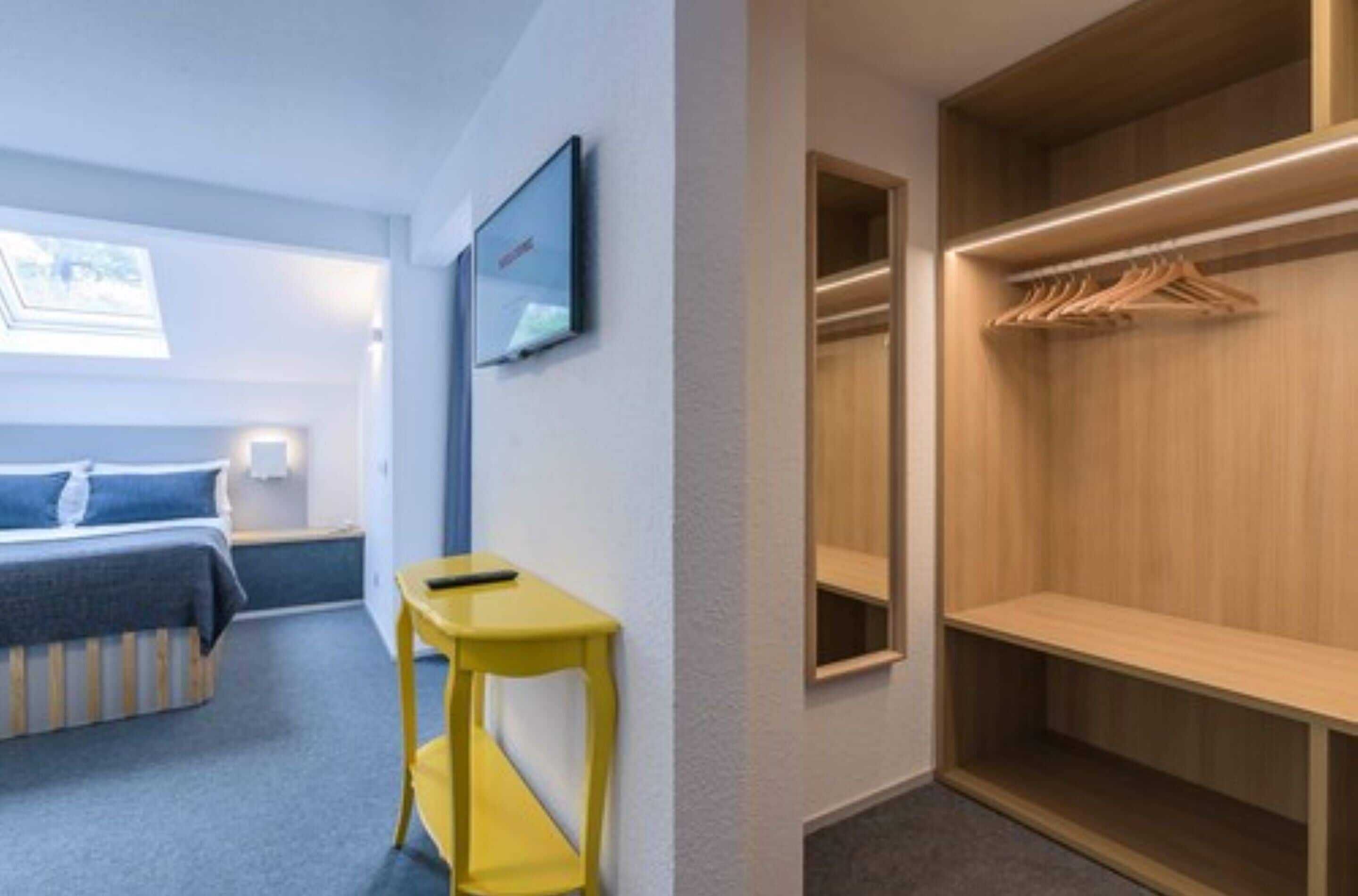 Una habitación de hotel con cama, una mesita, un armario y un televisor de pared.