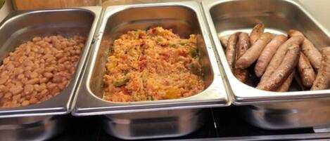 Un bufé con tres opciones de comida: frijoles, una cazuela de verduras y salchichas.