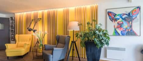 A modern living room with a yellow armchair, a gray armchair, a floor lamp, and a large potted plant.
