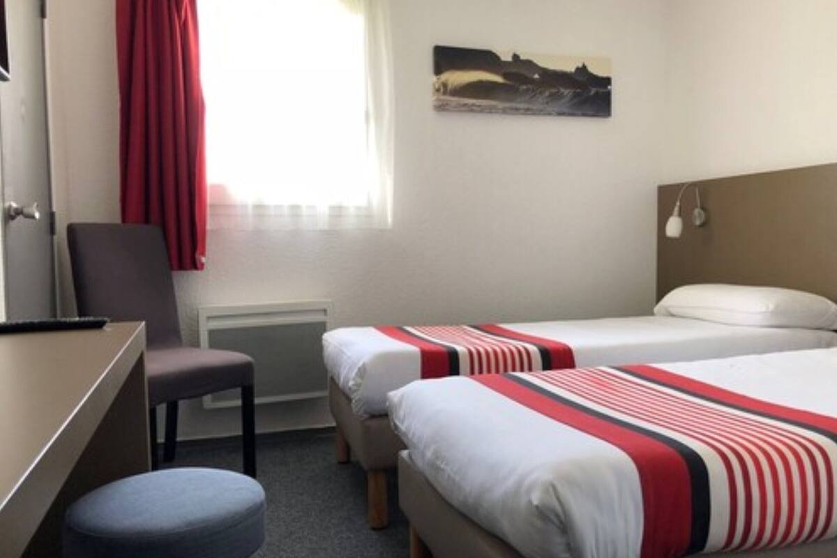 A hotel room with two beds, a desk, a chair, and a small stool.