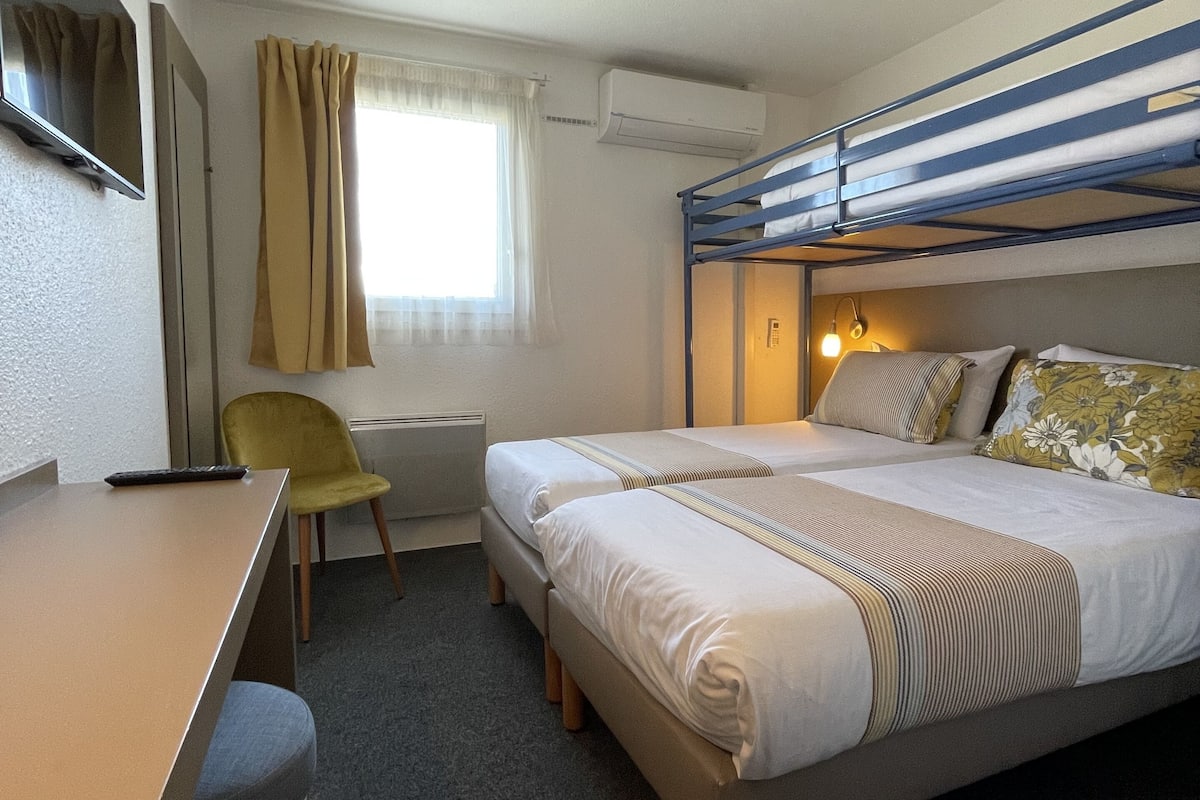 A compact hotel room with a bunk bed, a desk, a chair, and a TV.