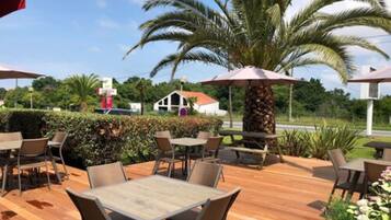 Une terrasse extérieure avec des tables et des chaises en bois, entourée de verdure et de palmiers.