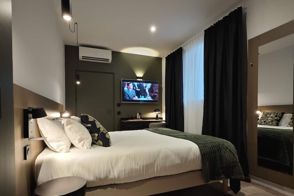 A modern hotel room with a large bed, a flat-screen TV, a bedside table, and a round black stool.