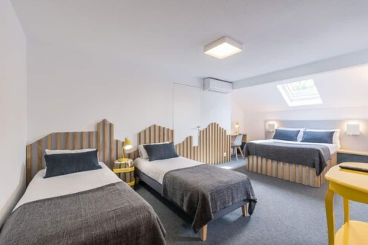 A hotel room with two single beds, a small desk, a chair, and a skylight.