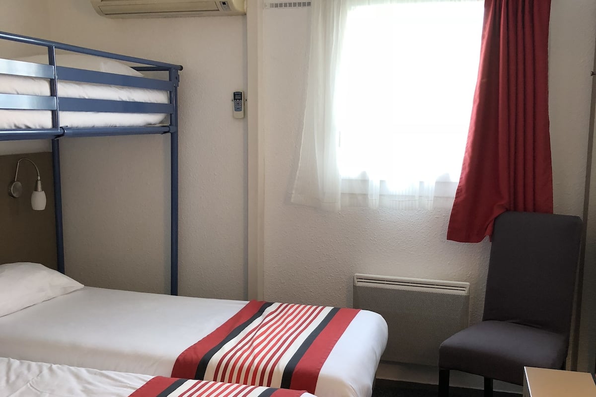 A hotel room with bunk beds, a desk, a chair, a radiator, and a window with curtains.
