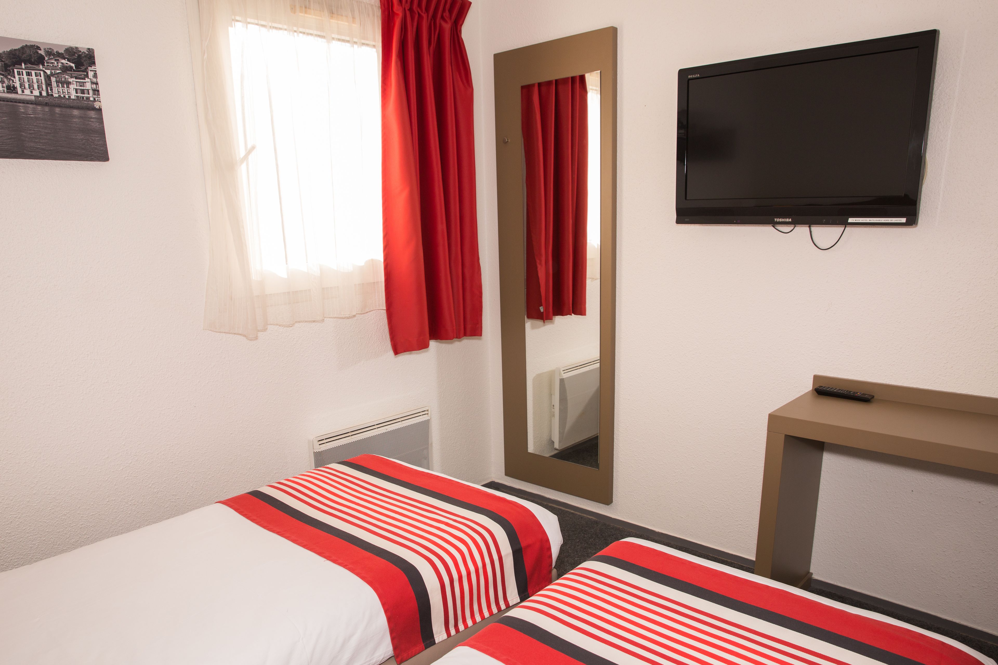 A hotel room with two beds, a TV, a desk, and a window with curtains.