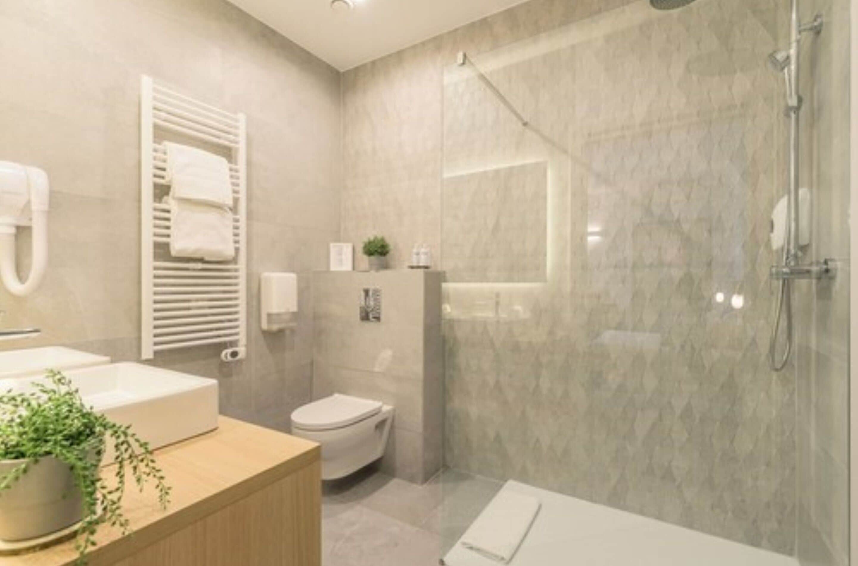 Un baño moderno con ducha de mármol, inodoro y lavamanos con una planta.