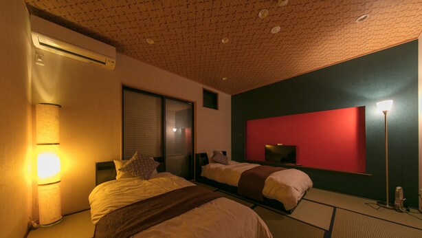 Habitación de hotel con dos camas, una pared de acento roja, un techo con diseño geométrico y una lámpara de pie.