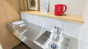 Un baño moderno con un lavamanos de acero inoxidable, una taza roja y un cuadro en la encimera.