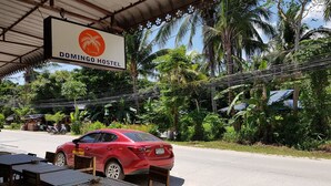 Un coche rojo estacionado frente al Hostal Domingo, con un letrero encima.