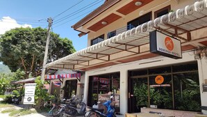 Un edificio con un letrero que dice 'Domingo Hostel' y un cartel de 'Habitación en alquiler'. Hay motocicletas estacionadas afuera y una mesa con sillas en la parte delantera del edificio.