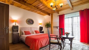 Une chambre avec un plafond en bois, un lit avec une literie rouge, une table de chevet, une chaise, une table avec un vase et une fenêtre avec des rideaux rouges.