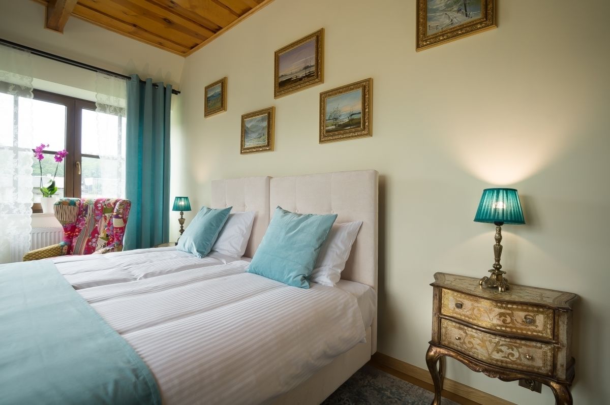 Een slaapkamer met een groot bed, een nachtkastje met een lamp en een stoel met een bloemenkussen.