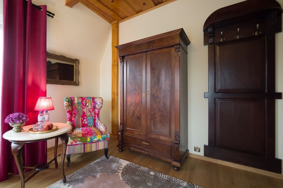 A room with a wooden cabinet, a colorful chair, a table with a lamp, and a red curtain.