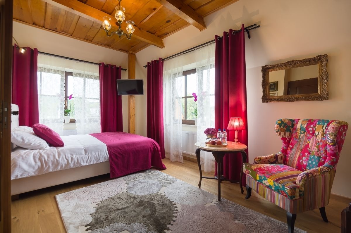 Un dormitorio con una cama, una silla, un televisor y una ventana con cortinas.