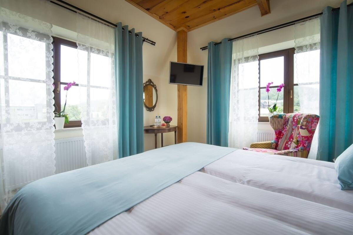 A bedroom with two beds, a TV, a small table with a mirror, and a chair with a floral cushion.