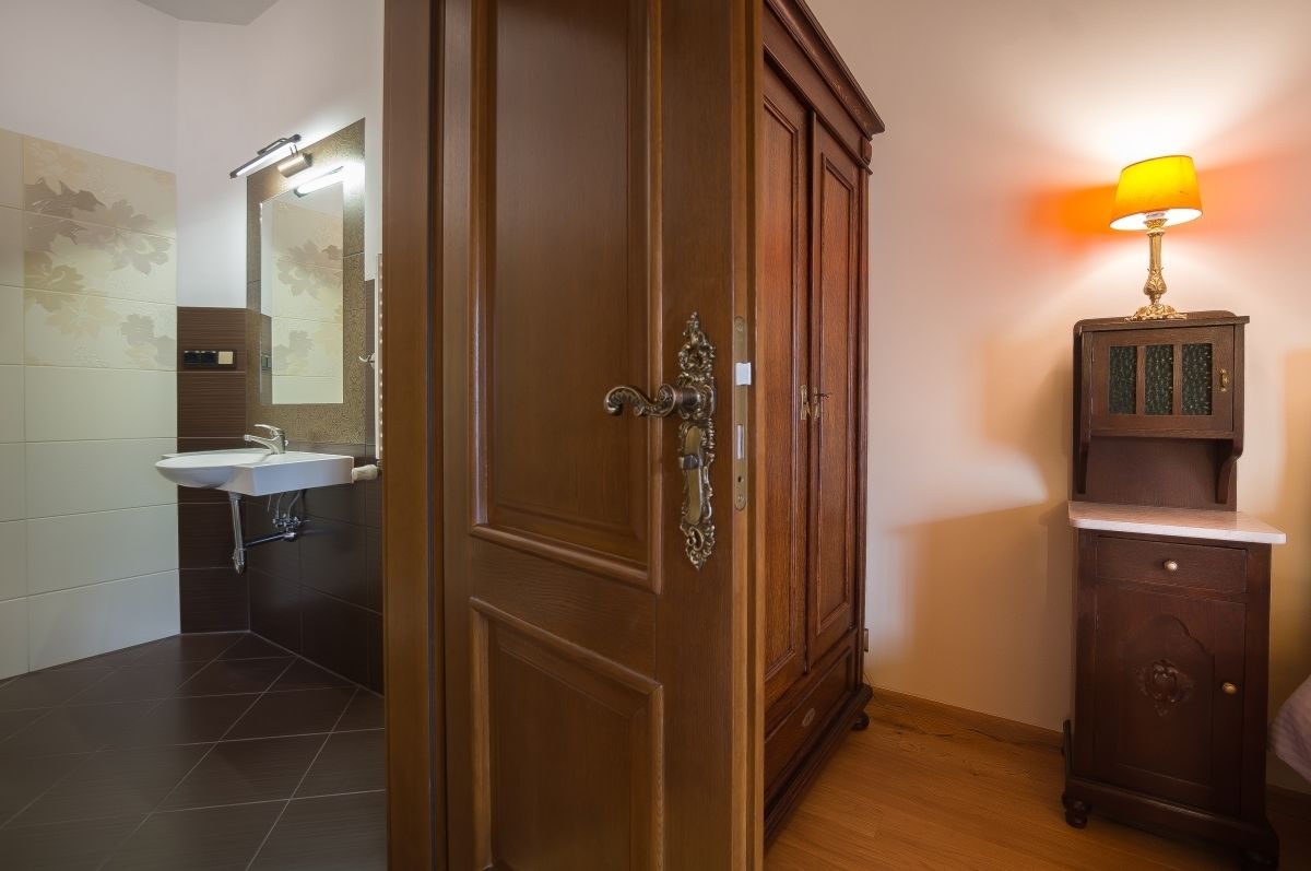 Un baño con puerta de madera, lavamanos, espejo y un mueble con lámpara.