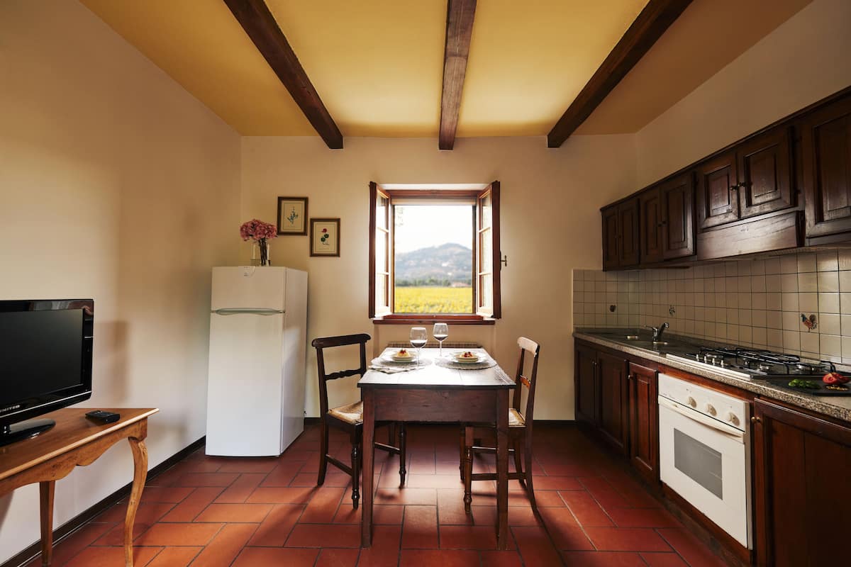 Una cocina con una mesa de comedor, sillas, un refrigerador, una estufa y una ventana con vista a un campo.