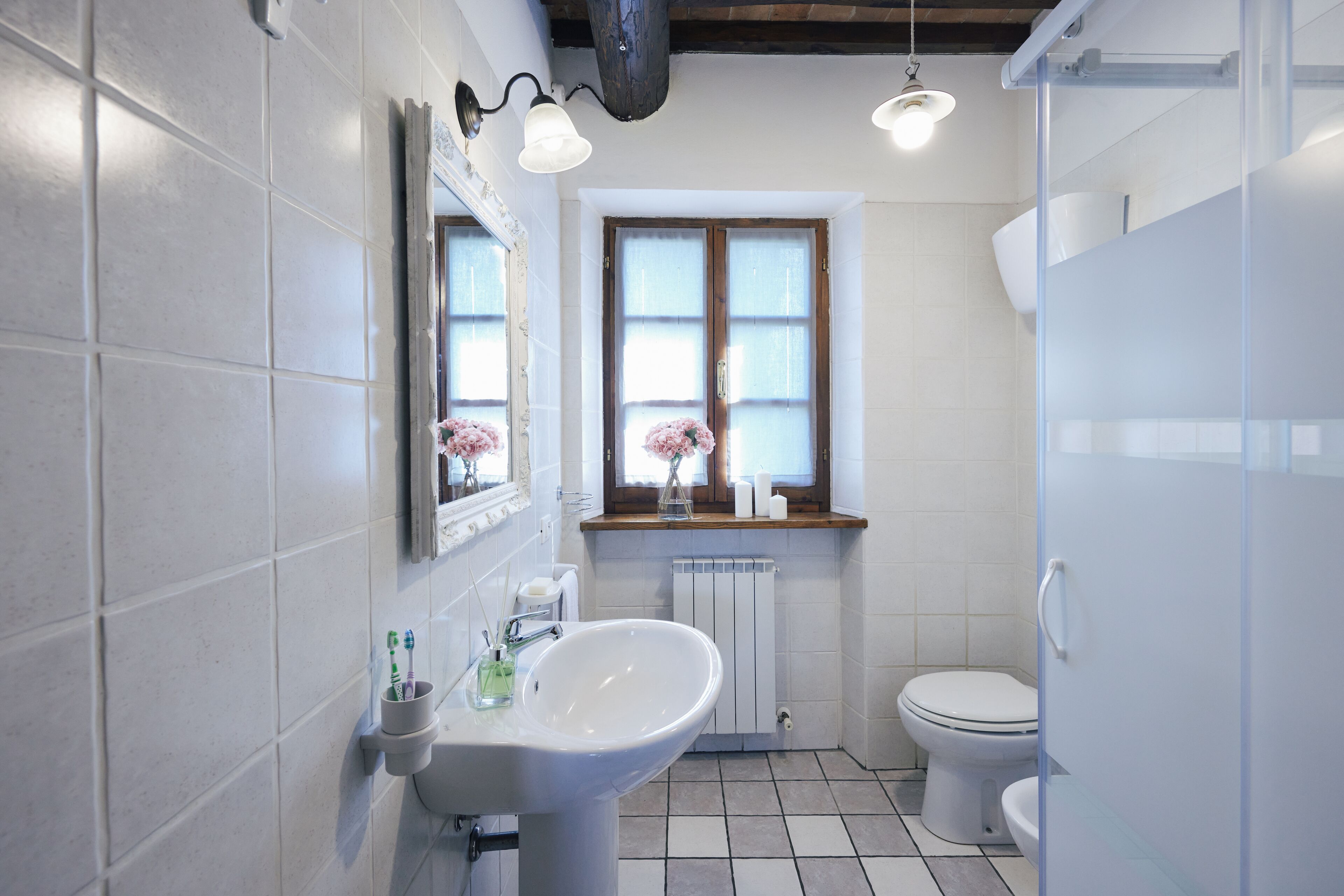 Une salle de bain avec un lavabo blanc, des toilettes, une fenêtre donnant sur un beau paysage et un espace douche.