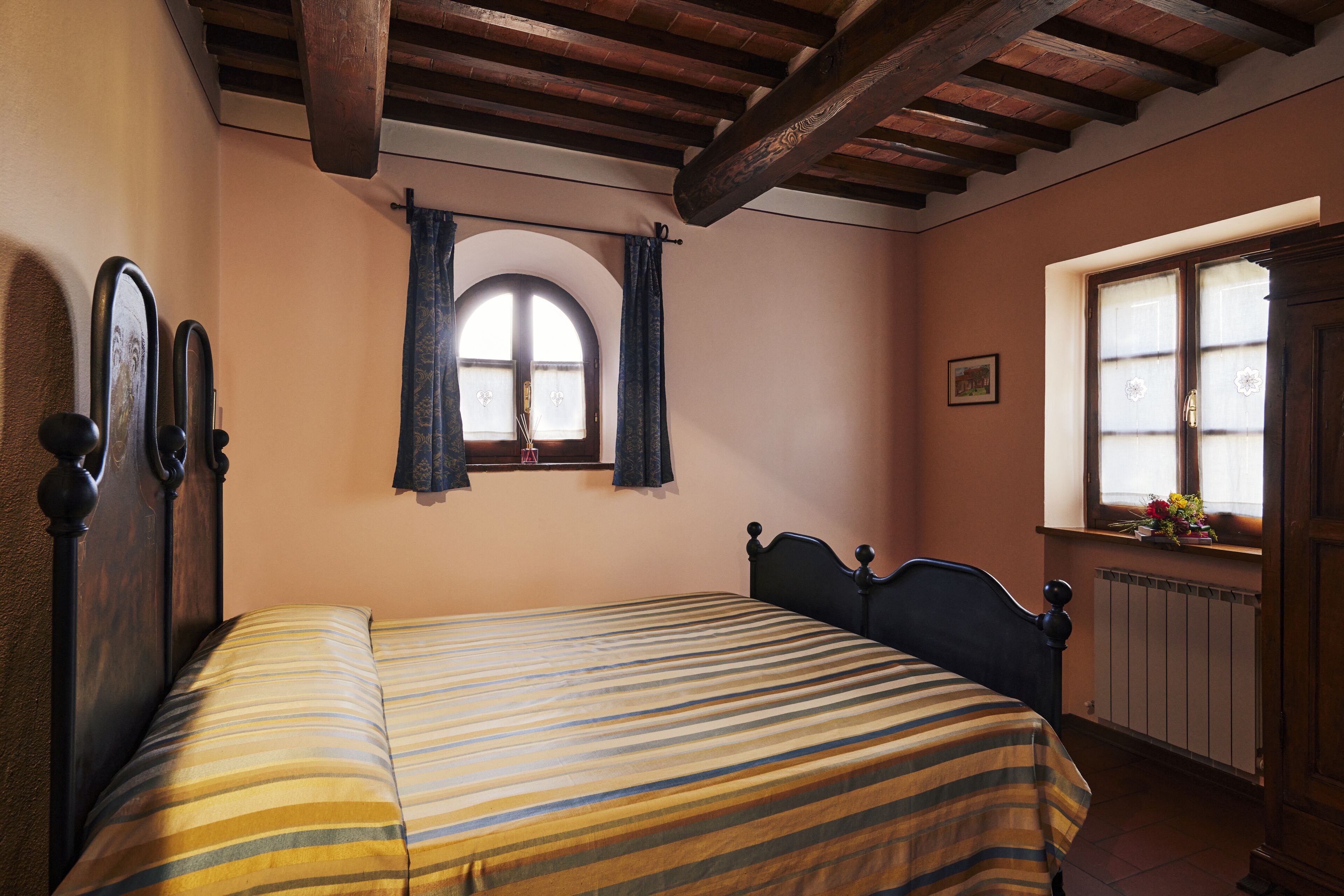 Ein Schlafzimmer mit Bett, einem Fenster mit Vorhängen, einem Heizkörper und einer Holztür.