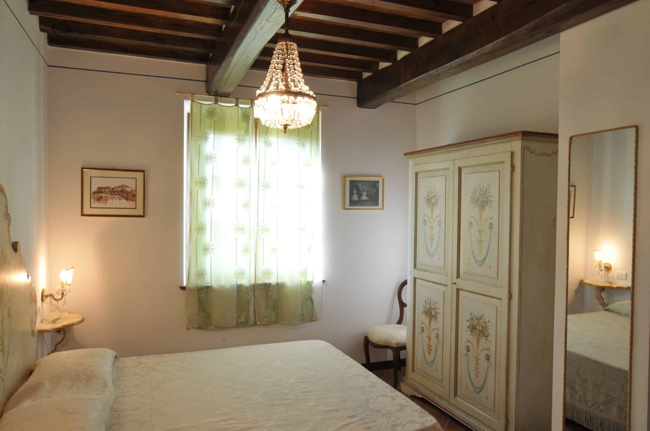 A bedroom with a bed, a chandelier, a cabinet with floral designs, and a mirror.