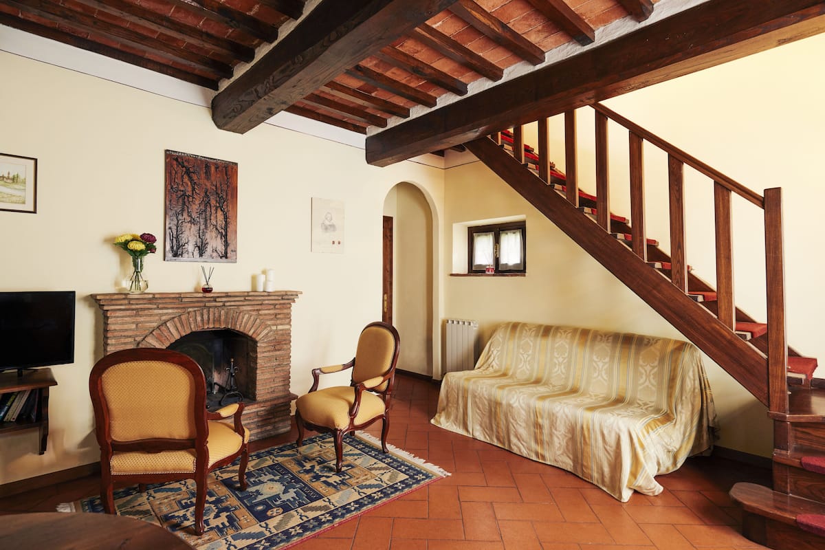Una sala de estar con chimenea, un sofá, una escalera de madera y un televisor.
