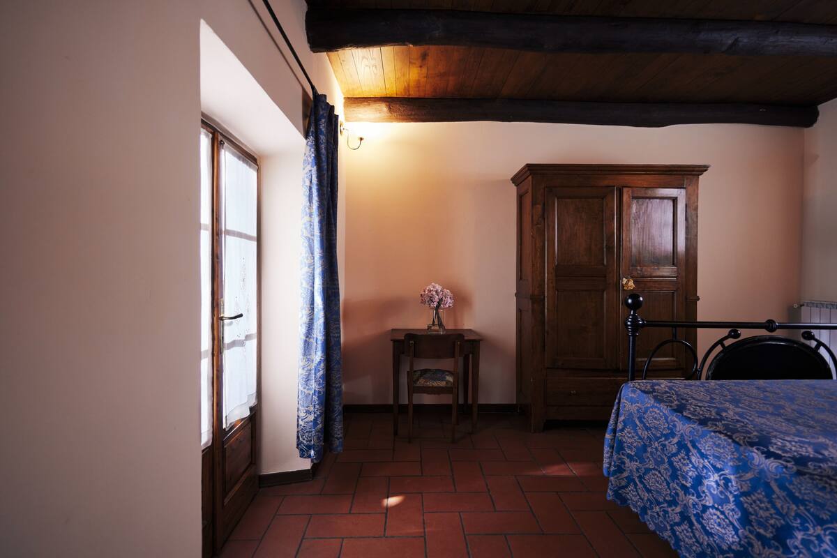 Un dormitorio con una cama de madera, una mesita con un florero y un armario.
