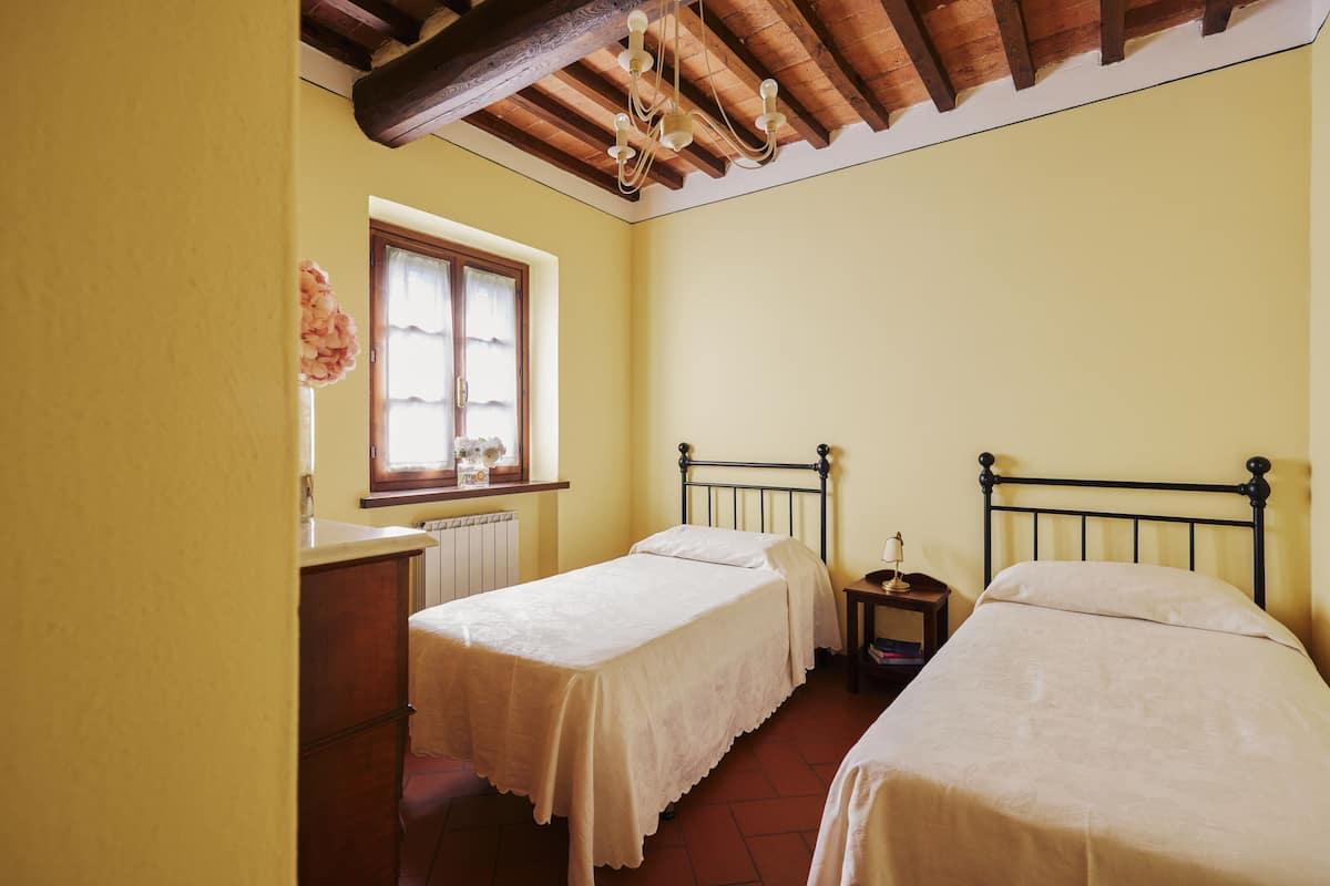 Una habitación pequeña y acogedora con dos camas individuales, techo de madera y ventana con cortinas.