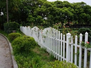 A white picket fence with lush greenery and trees in the background.