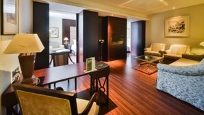 A hotel room with a wooden floor, a sofa, a chair, a small table, and a lamp. There is a painting on the wall and a door leading to another room. - Grand Inn Xijiao State Guest Hotel (Shanghai)